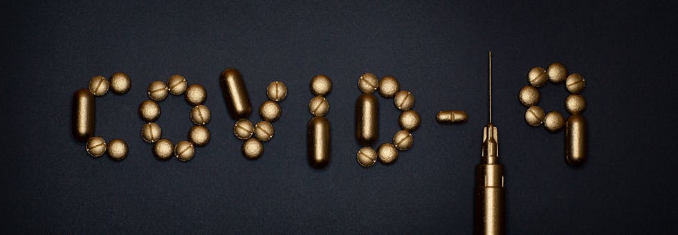 Artistic depiction of COVID-19 using pills and a syringe on a dark background, symbolizing medication.