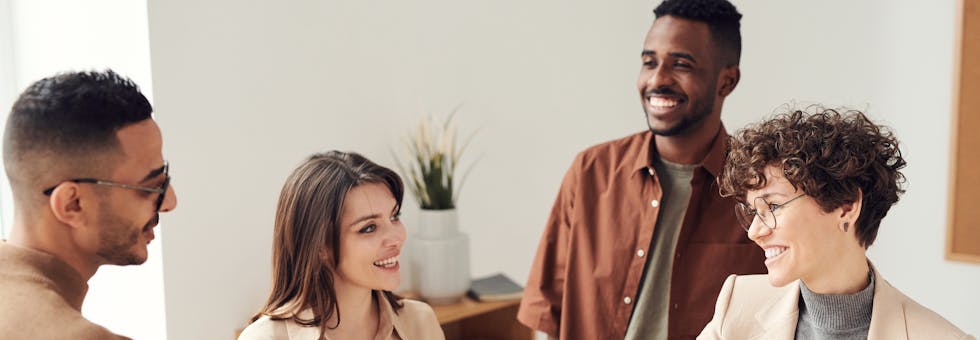 Four colleagues smiling and shaking hands in a bright office setting.